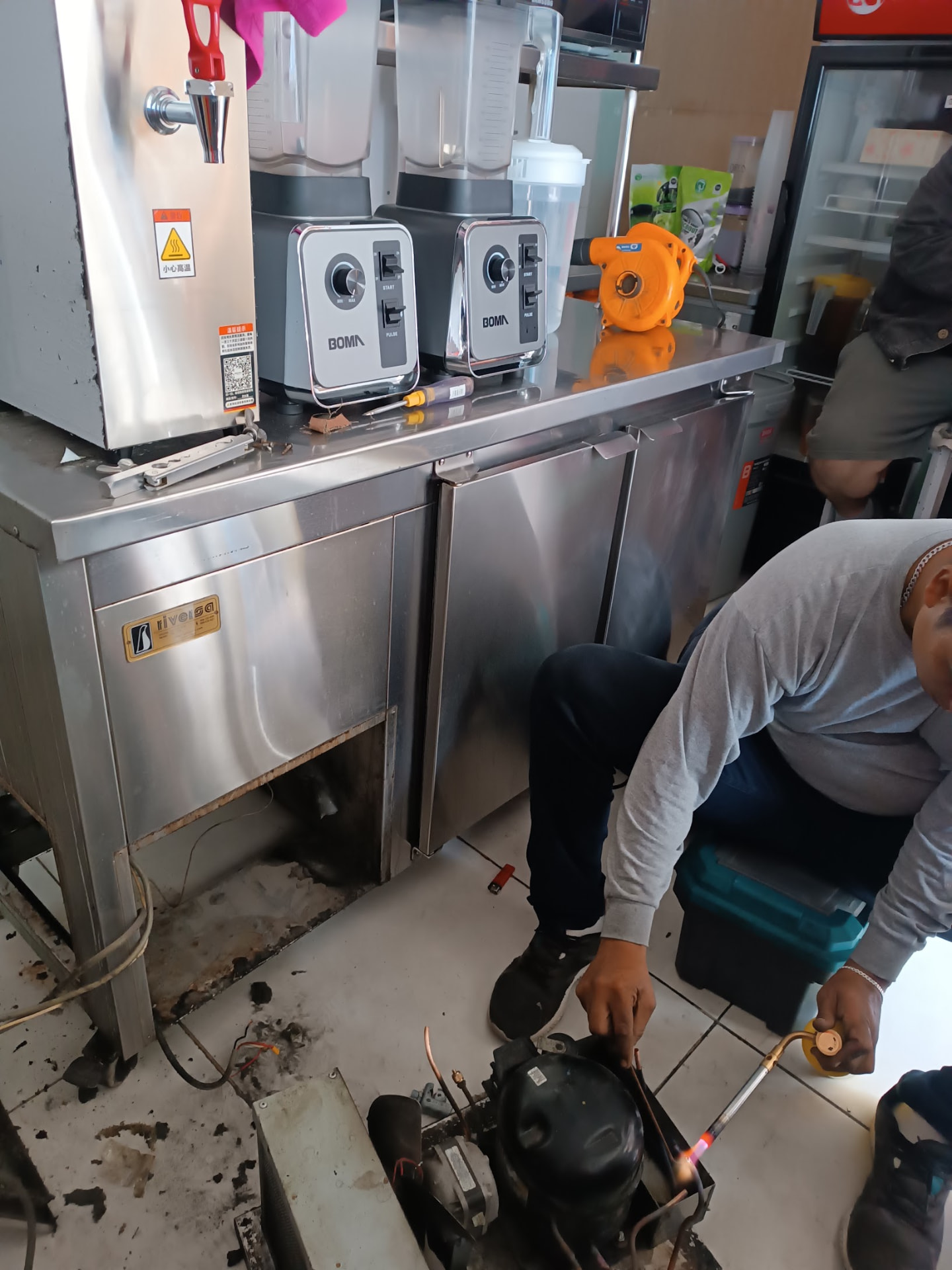 Técnico soldando el compresor de una mesa refrigerada en cafetería de Lima